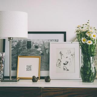 A stylish interior setup featuring a lamp, art frames, and a vase of flowers on a tabletop.
