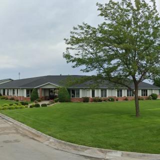 A suburban house with a well-maintained lawn and tree under a cloudy sky.