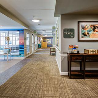 A modern office hallway with carpet flooring, artwork on the walls, and office furniture.