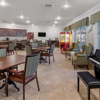 A spacious community room with tables, chairs, a television, and recreational items like a popcorn machine and piano.