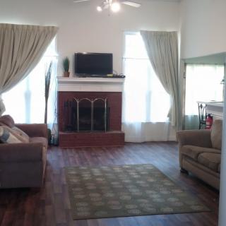 A cozy living room featuring a fireplace, sofa, armchair, television, and large windows with curtains.