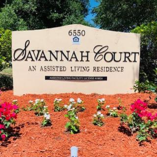 The entrance sign for Savannah Court, an assisted living residence, surrounded by vibrant flowers.