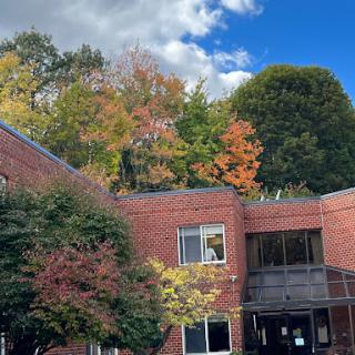 A peaceful autumn scene featuring a brick building surrounded by colorful trees under a bright blue sky.
