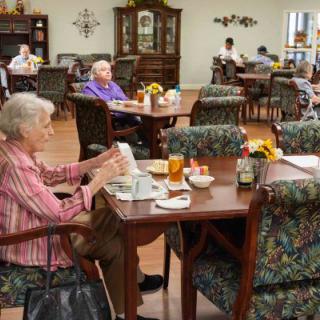 Elderly residents enjoying a meal in a senior living community dining hall.