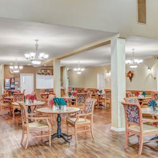 A spacious dining area with multiple tables and chairs, illuminated by chandeliers, featuring a wooden floor.