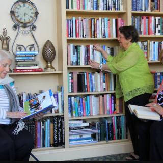 People in a library setting, reading and organizing books on the shelves.