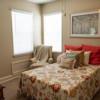 A cozy bedroom with a floral bedspread, decorative pillows, and natural lighting.