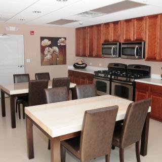 A modern kitchen and dining area featuring multiple tables and chairs, with stoves and wooden cabinets.