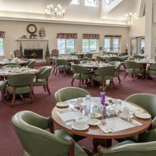 A spacious dining room with multiple tables set for a meal, featuring green chairs and large windows.