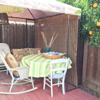 A cozy outdoor patio with a rocking chair and table under an umbrella, next to a lemon tree.