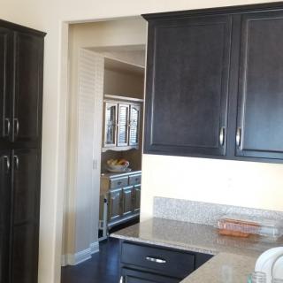 A modern kitchen with dark wood cabinets and a glimpse into an adjoining room.