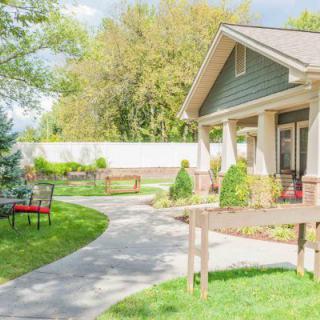 A cozy house with a well-maintained garden and a winding pathway, surrounded by lush greenery and outdoor seating.