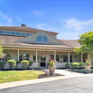 A charming residential building with a large front porch and landscaped yard on a sunny day.
