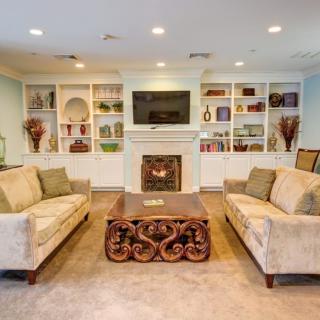 A cozy living room with elegant furniture, featuring sofas, a decorative coffee table, built-in shelves, and a fireplace topped with a television.