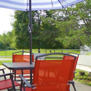 A cozy outdoor setup featuring red patio chairs and an umbrella, surrounded by lush greenery.