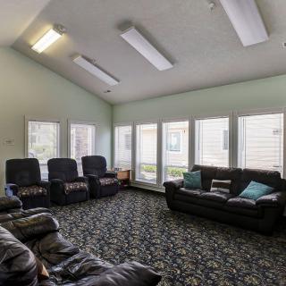 A spacious living room with multiple sofas and armchairs, featuring large windows and a patterned carpet.