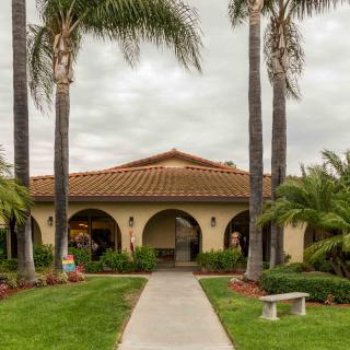 A Mediterranean-style building with a tiled roof and arches, surrounded by palm trees and a well-maintained garden path.