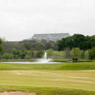 A scenic view of a golf course with a fountain and distant building.