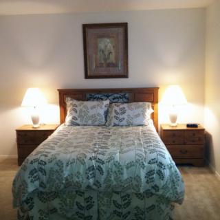 A cozy bedroom featuring a neatly made bed with patterned bedding, flanked by two nightstands with lamps and a framed artwork above the headboard.