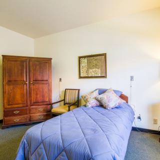 A minimalist bedroom featuring a single bed with blue bedding, a wooden wardrobe, and an armchair.