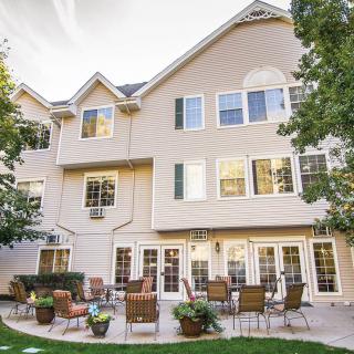 A cozy backyard patio area with seating arrangements adjacent to a multi-story house.