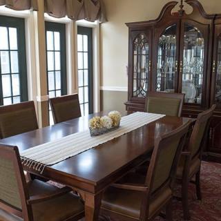 A classic dining room featuring a wooden table, chairs, and a china cabinet against large windows.