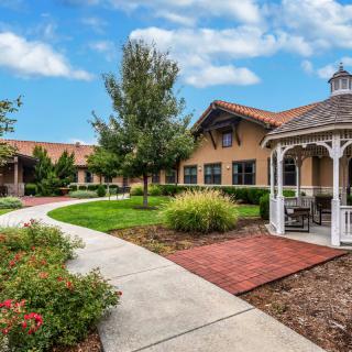 A peaceful courtyard with a gazebo and well-maintained landscaping, featuring a winding pathway under a partly cloudy sky.