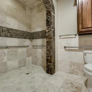 A spacious, accessible bathroom with tiled walls, featuring a walk-in shower and grab bars for safety.