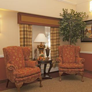 A cozy living room setup with two patterned armchairs, a small table with a lamp, and decorative elements including a plant and artwork.
