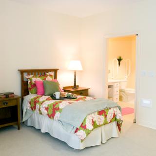 A cozy bedroom featuring floral bedding, a bedside lamp, and an inviting bathroom entrance.