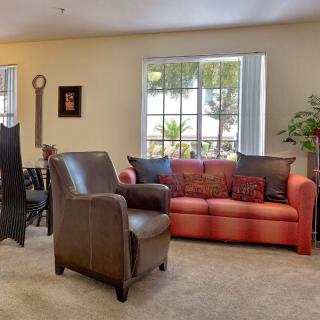 A cozy living room with a red sofa and brown armchair, adjacent to a dining area.