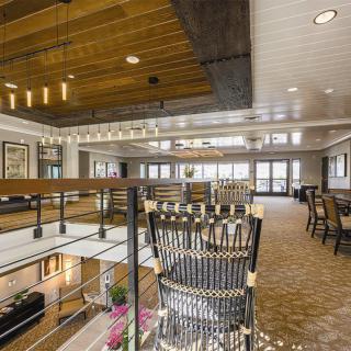A modern dining area with elegant chandeliers and stylish seating, featuring a wooden ceiling and balcony overlook.