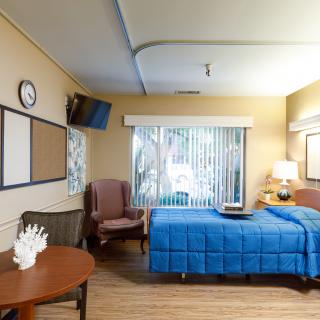 A well-lit hospital room with a single bed, TV, and seating area.