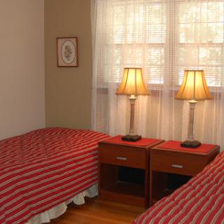 A cozy bedroom featuring twin beds with striped red bedspreads and classic nightstands with lamps.