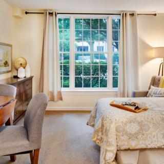 A cozy bedroom with a large window letting in natural light, featuring a comfortable bed, a desk with a chair, and stylish decor.