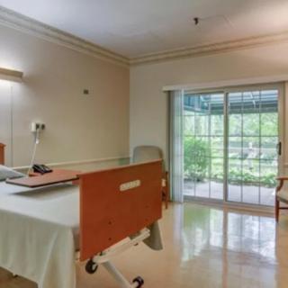 A clean and well-lit hospital room with a patient bed and a large window overlooking greenery.