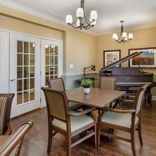 A cozy dining room featuring a grand piano, elegant chandeliers, and French doors.