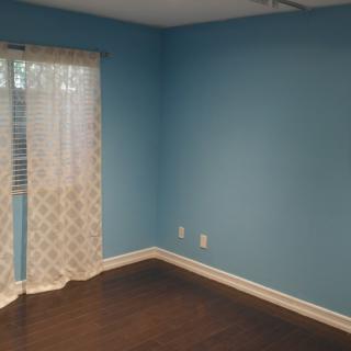 A brightly lit room with blue walls, dark wood flooring, and patterned curtains.
