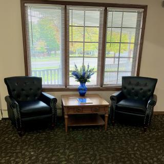 A cozy seating area with two leather chairs, a wooden coffee table, and a vase of flowers by a large window.