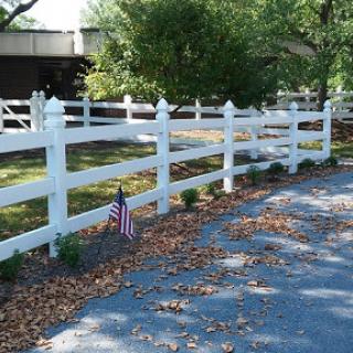 A neatly maintained white fence along a gravel pathway, complemented by seasonal leaves and an American flag.