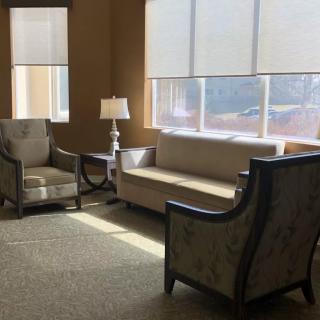 A cozy living room with a sofa, armchairs, and a lamp near large windows.