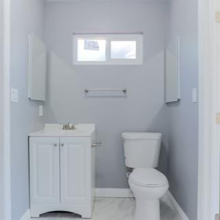 A minimalist bathroom featuring a toilet, sink, and small window.