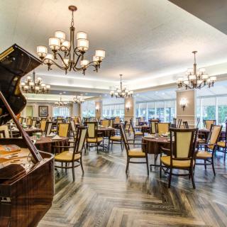 An elegant dining room with a grand piano, chandeliers, and neatly arranged tables and chairs.
