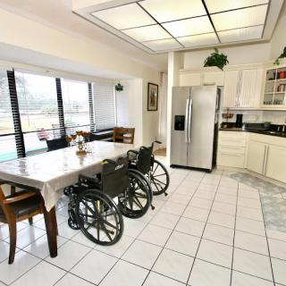 A modern kitchen and dining area with wheelchairs by the table, featuring a large refrigerator and white tiled flooring.