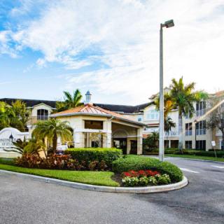 A well-maintained residential entrance with palm trees and lush landscaping under a sunny sky.