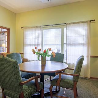 A cozy dining room with a round table, chairs, and a vase of flowers by the window.