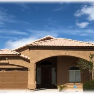 A suburban house with a tile roof and an arched entryway under a clear blue sky.