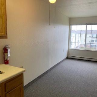 An empty room with a window, kitchen counter, and a fire extinguisher on the wall.