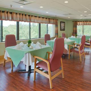 A well-lit dining area featuring neatly arranged tables with green tablecloths and comfortable chairs, surrounded by large windows.