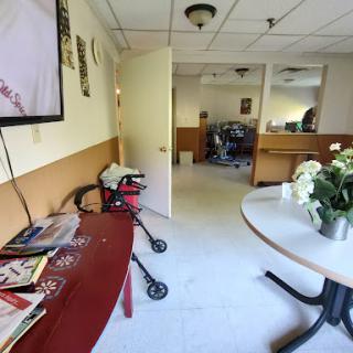 A view of a brightly lit interior room featuring a table with flowers, a television on the wall, and a reception area with various magazines.